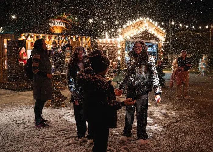 Visitors enjoying falling snow among the market stalls at night